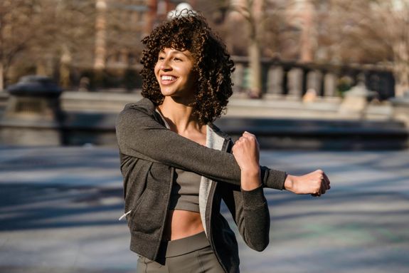 Content young ethnic female athlete in sportswear with curly hair working out while looking away on sunny street