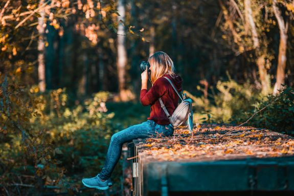 Young woman takes photos in a vibrant forest setting, embracing nature.