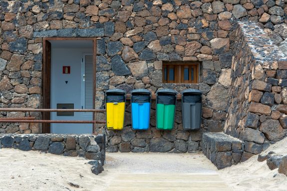A stone wall with three trash cans in front of it
