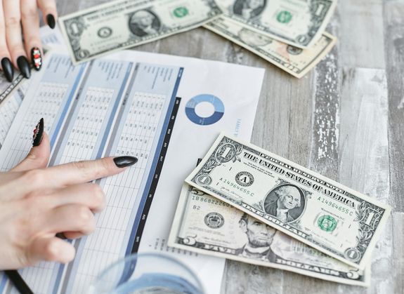 Close-up of hands analyzing financial document with US dollar bills on table.