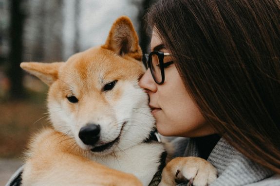 A woman lovingly embraces and kisses her Shiba Inu dog outdoors.