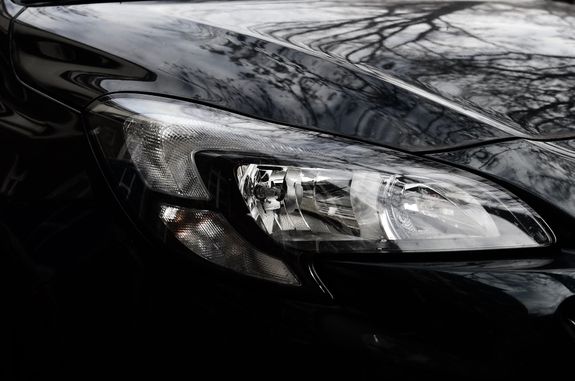 Polished reflecting surface of black modern car hood with glossy headlight on street