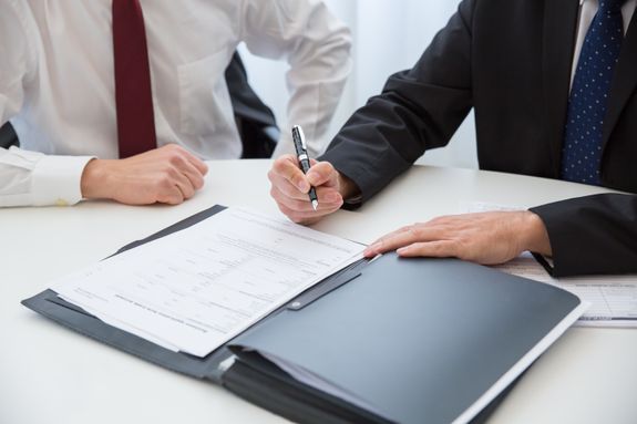 A Person in Black Suit Holding a Pen Near the Documents on the Table