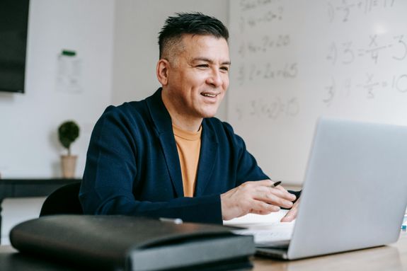 Smiling professional man engaged in remote work using a laptop in a modern office setting.