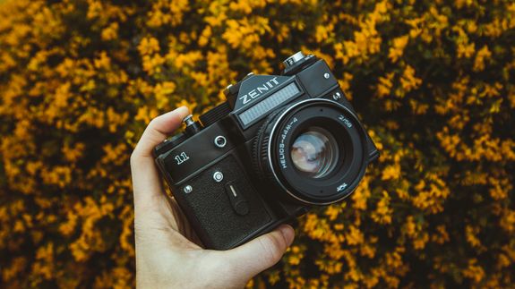 Close-up of a Zenit camera held against a vibrant yellow floral background, showcasing vintage photography equipment.