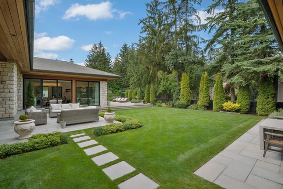 Exterior of contemporary residential house with balcony and cozy terrace with couch near trees on green yard on daytime