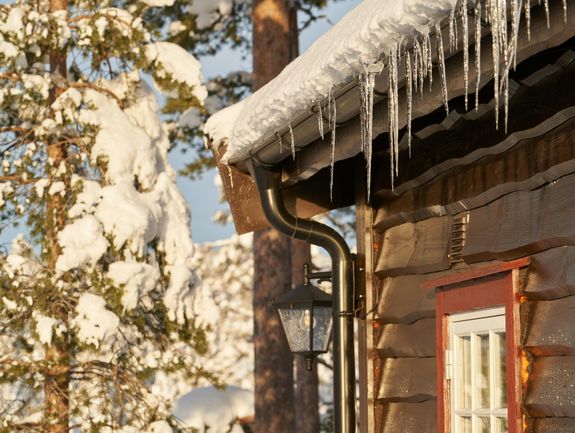 Cozy wooden cabin with icicles on the roof, set in a snowy forest.