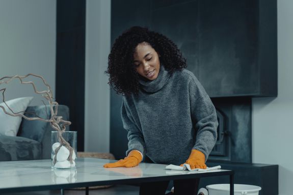 African American woman cleaning a table with orange gloves in a cozy, modern living room setting.