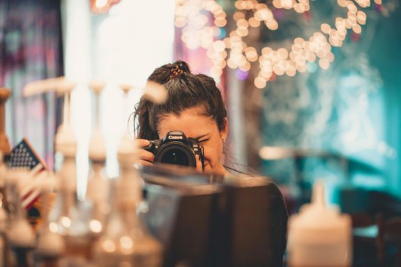 A woman photographer takes a picture indoors with festive lights and an American flag in the background.