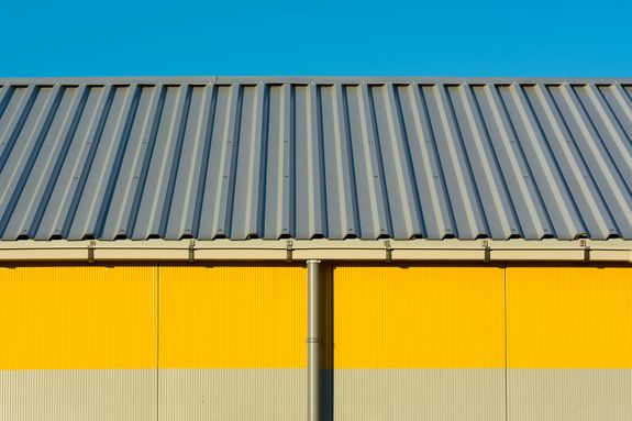 Photo of a yellow warehouse wall with a corrugated metal roof under a clear blue sky.