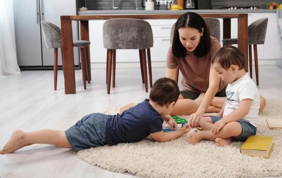 Mother and two kids playing together on the rug at home, enjoying family bonding time.