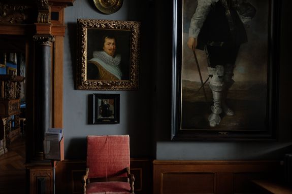 Interior of modern art gallery with portraits in cozy frames hanging on blue wall near comfy old chair