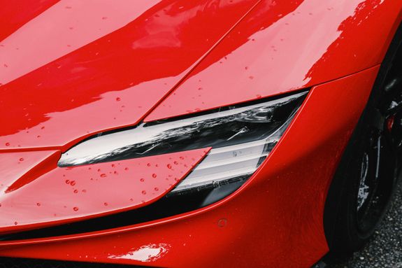 Detailed view of a sleek red sports car headlight with water droplets enhancing its glossy finish.