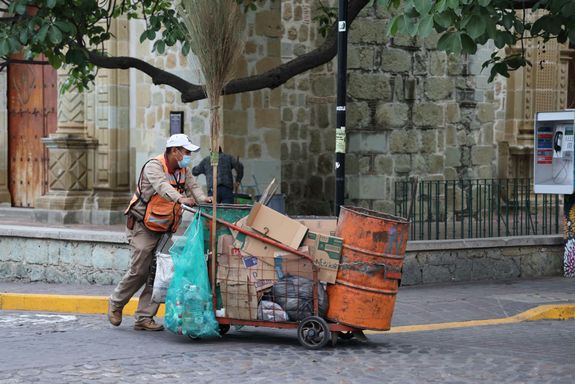 Street cleaner in Oaxaca De Juárez pushes cart with tools, showcasing urban life.