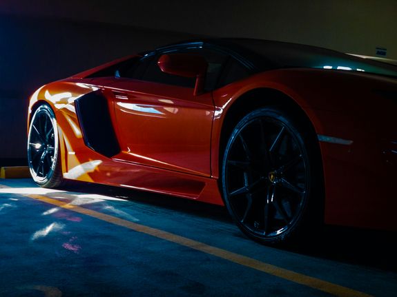 Close-up of a vibrant orange sports car parked in a sunlit garage, showcasing luxury and modern design.