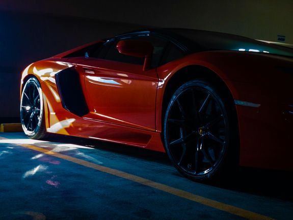 Close-up of a vibrant orange sports car parked in a sunlit garage, showcasing luxury and modern design.