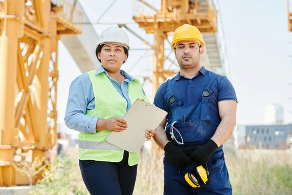 Man in Blue Shirt Wearing Yellow Hard Hat Standing beside a Woman in Blue Long Sleeve Shirt