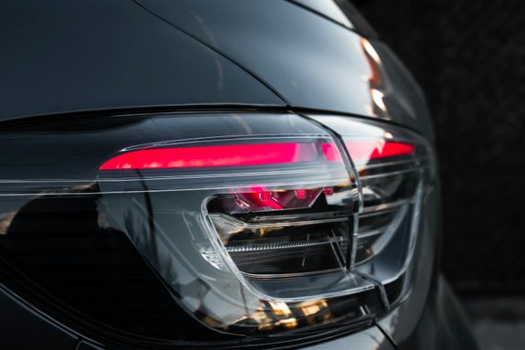 Detailed view of a sleek black car's taillight with red illumination, reflecting dusk light.