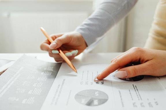 Hands holding a pencil, analyzing charts and data sheets, suggesting teamwork in an office setting.