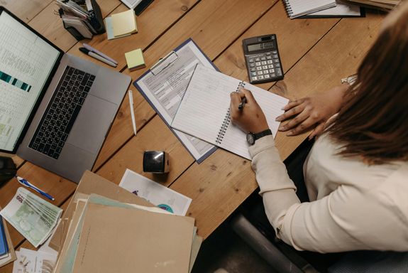 Focused woman calculating figures at office desk with a laptop and documents.