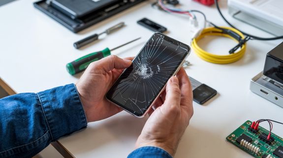 Close-up of a broken smartphone with a cracked screen on a leather car seat.