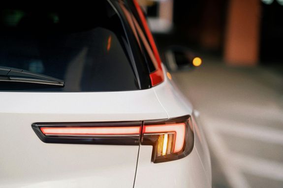 Detailed rear view of a car taillight with red and amber lights in a parking lot.