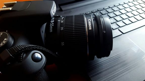 Close-up of a black DSLR camera with lens on a laptop keyboard.