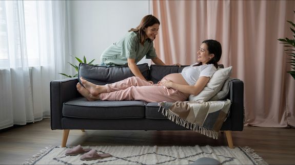 From above of crop faceless couple in casual outfit standing in light living room and touching pregnant belly gently