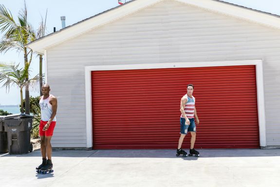 Two Men Roller Skating Near a Building with Red Roller Shutter