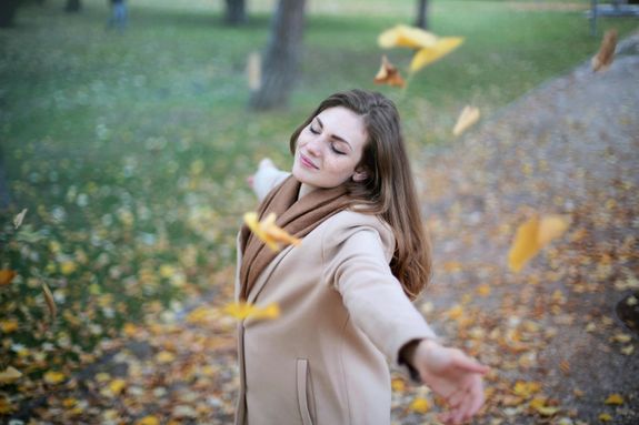 Young woman with arms outstretched, delighting in fallen leaves in a Paris park during autumn daytime.