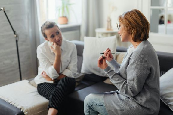 Two women, one being a therapist, engaging in a thoughtful conversation on a couch in a cozy room.