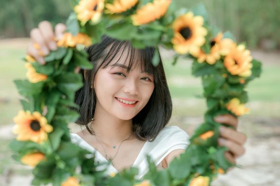 Young cheerful ethnic female demonstrating colorful sunflower wreath while looking at camera in park