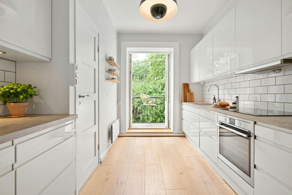 A long white kitchen with wooden floors and a window