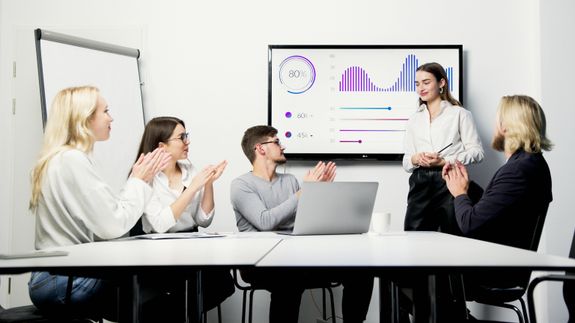 A Group of People Clapping to a Woman Presenting a Graph on Screen with Success Rate