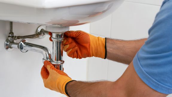Close-up of a person's hand turning a chrome faucet handle in a modern bathroom setting.