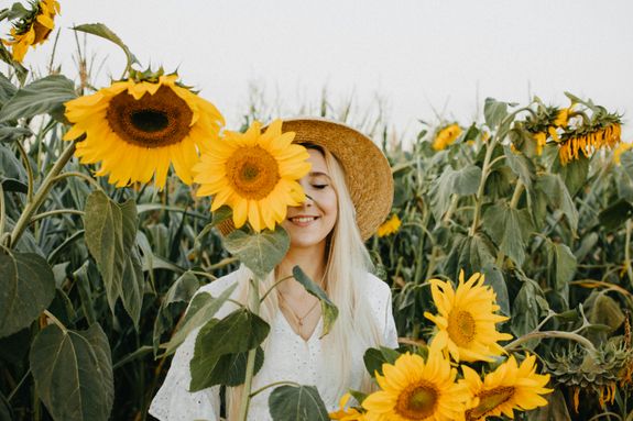 Smiling woman wearing straw hat surrounded by vibrant sunflowers in a field.