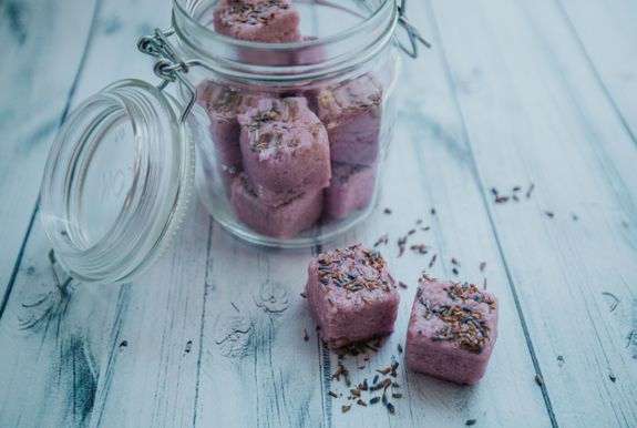 Aromatic purple bath bombs in glass jar arranged on white table