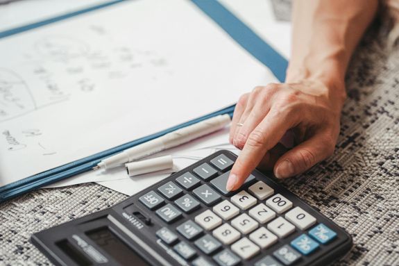 A hand using a calculator on top of documents, indicating financial calculation or analysis.