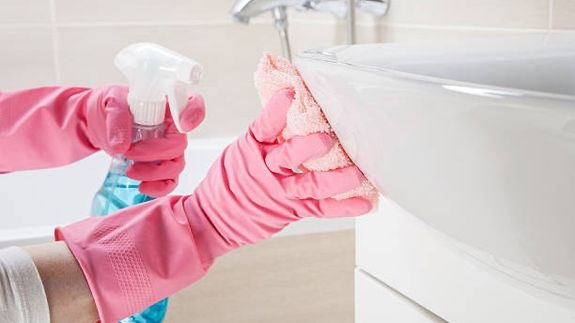 From above of crop faceless person in yellow gloves cleaning handle of cabinet with microfiber cloth in modern bright bathroom