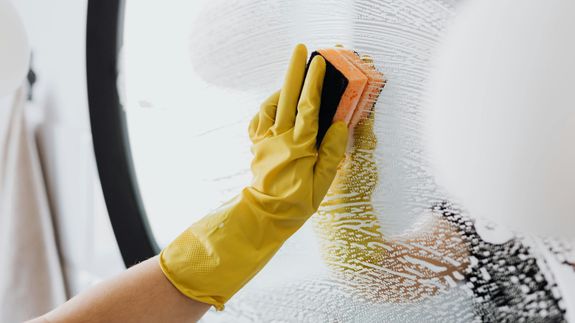 A professional cleaner in protective gear vacuuming the floor in a modern living room.