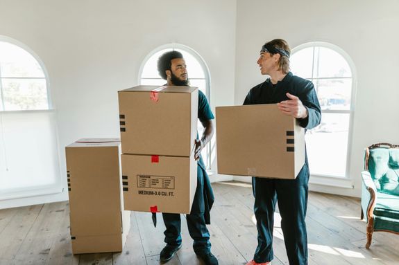 Woman in Purple Long Sleeve Shirt and Orange Pants Holding White Cardboard Box