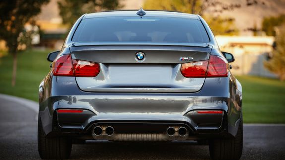 Close-up of a sleek black car's taillight with glowing red light during sunset, emphasizing design.