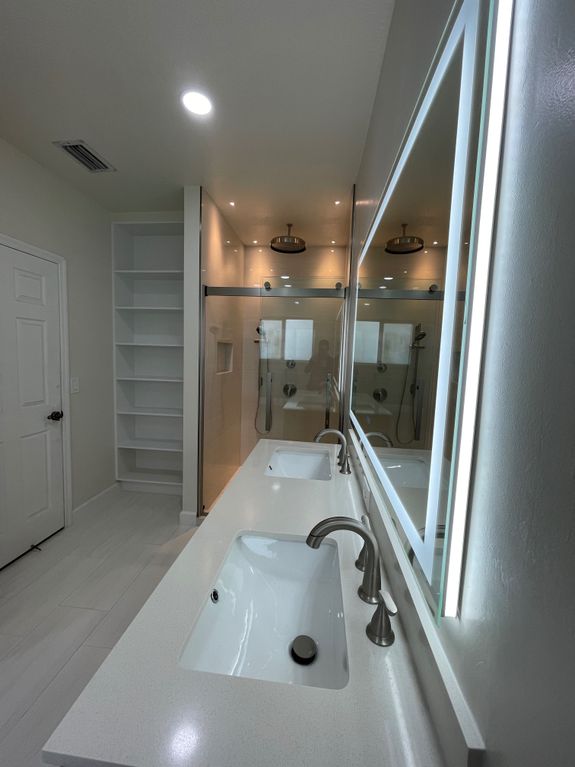 Interior of bathroom table with soap and cosmetic oil placed near white sink and faucet under mirror in wooden frame in modern apartment